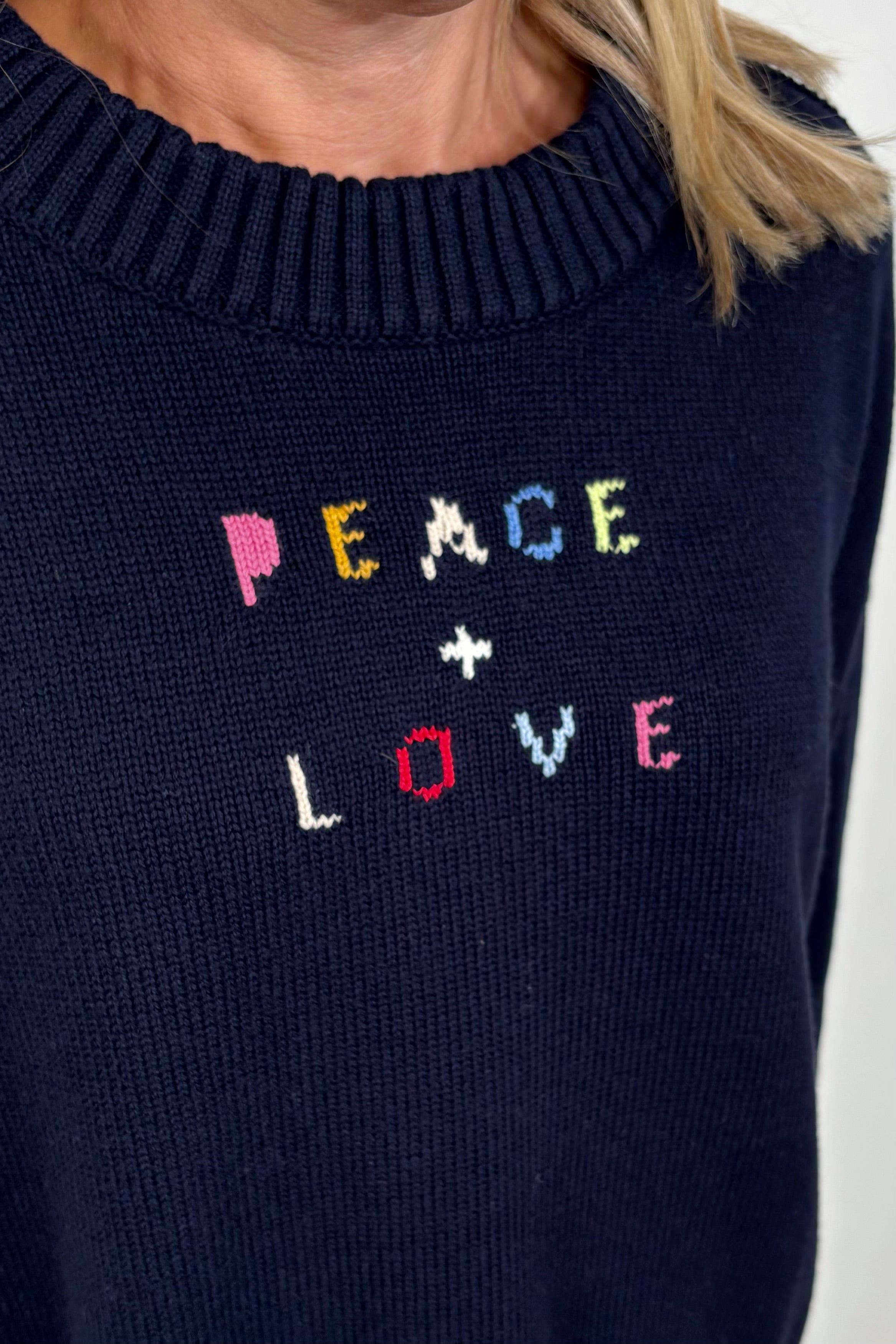 Close-up of a navy blue sweater with “Peace & Love” embroided