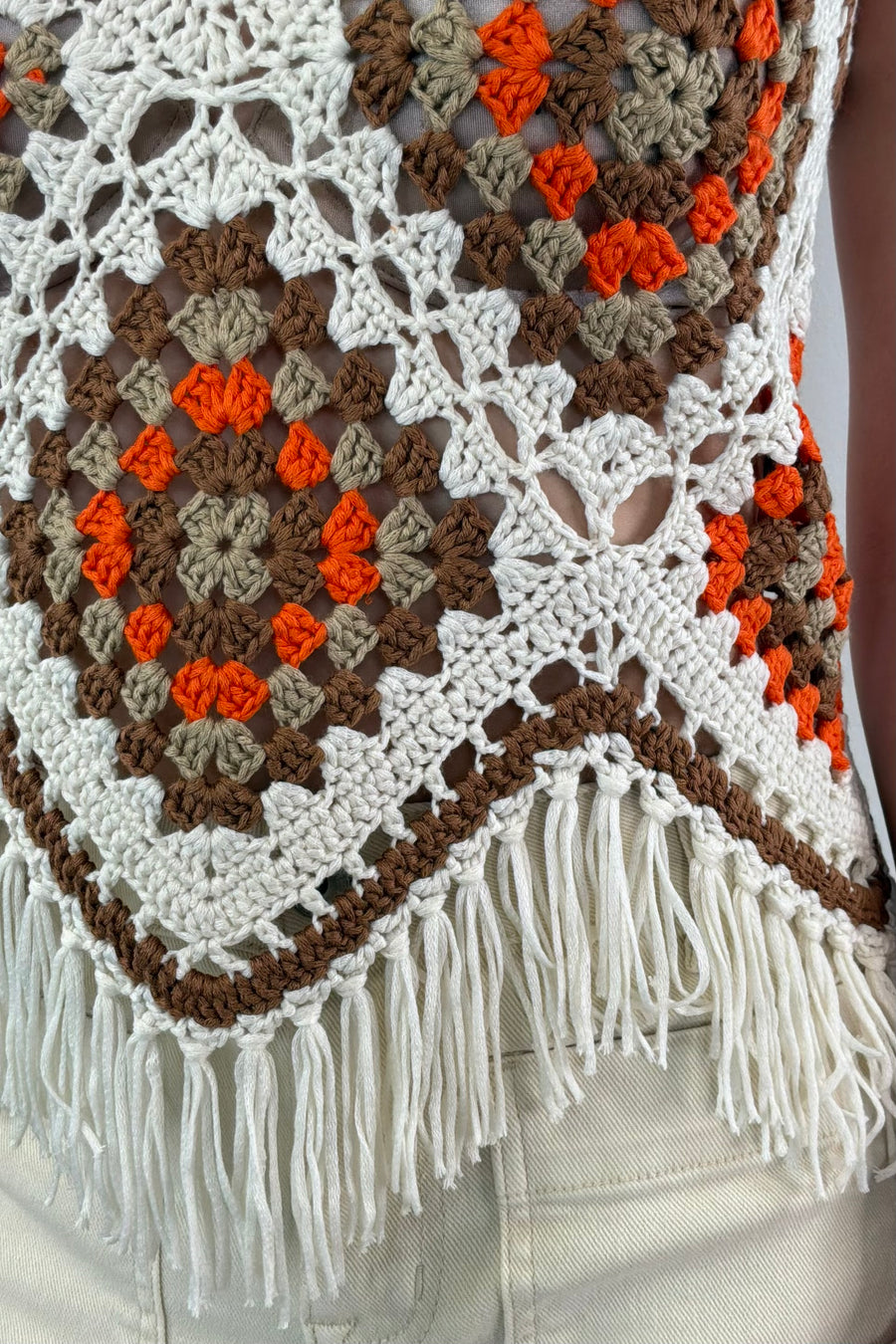 close-up of a white, beige, orange and brown crochet frayed tank top