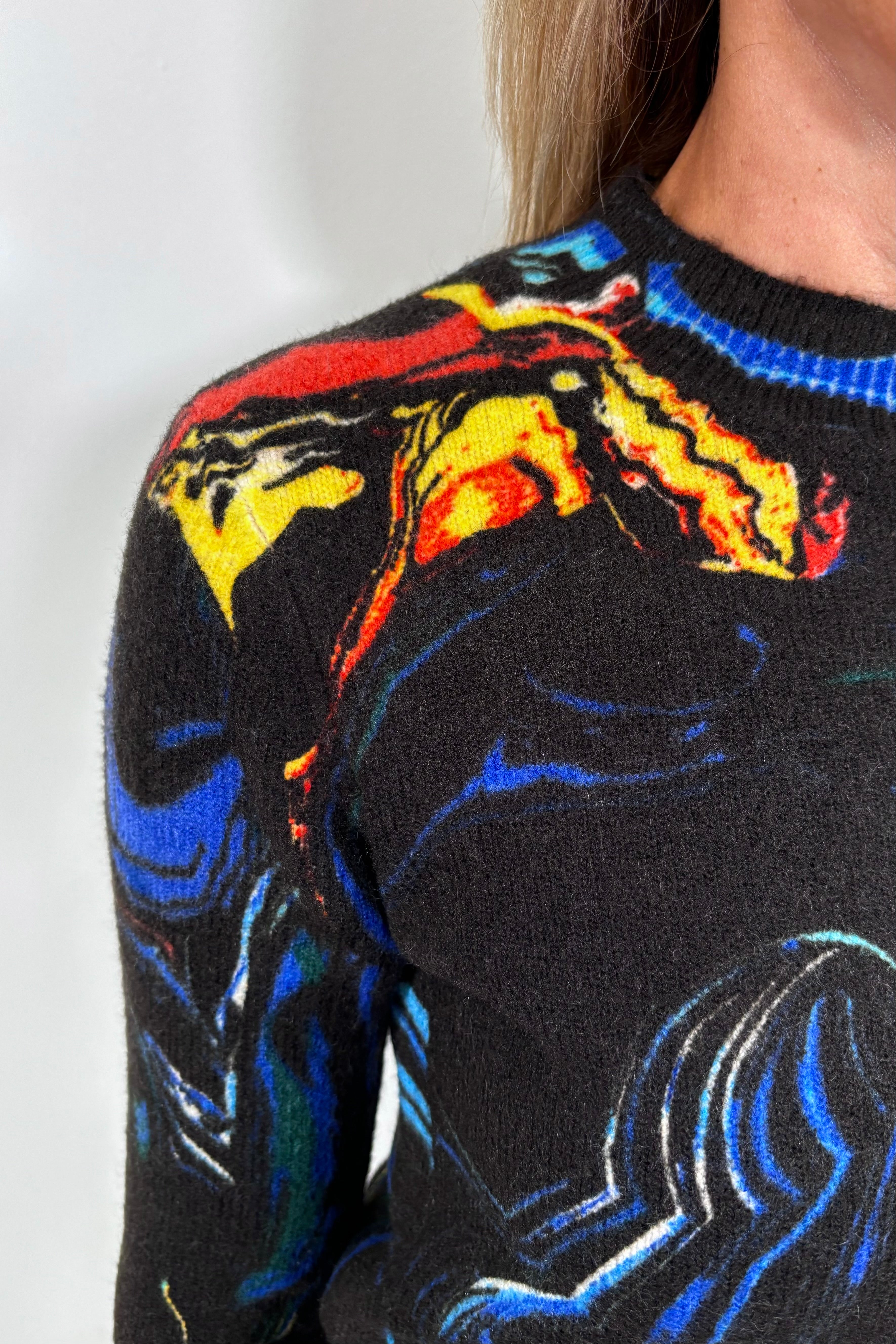 Close-up of a black sweater with colorful abstract patterns on a plain background