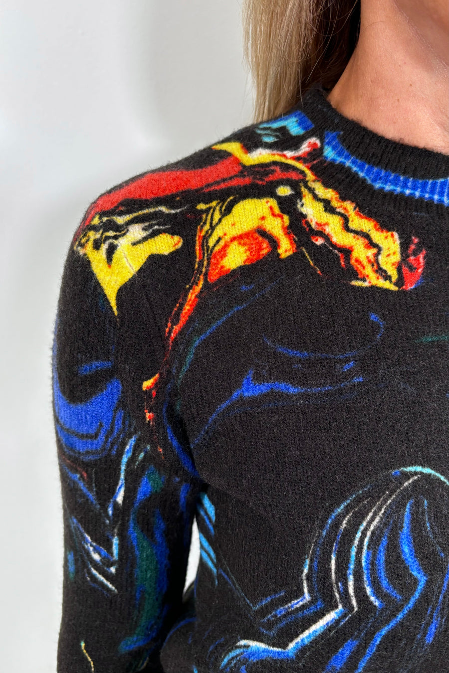 Close-up of a black sweater with colorful abstract patterns on a plain background