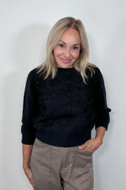 Front view of woman wearing a floral detailed sweater with pearls