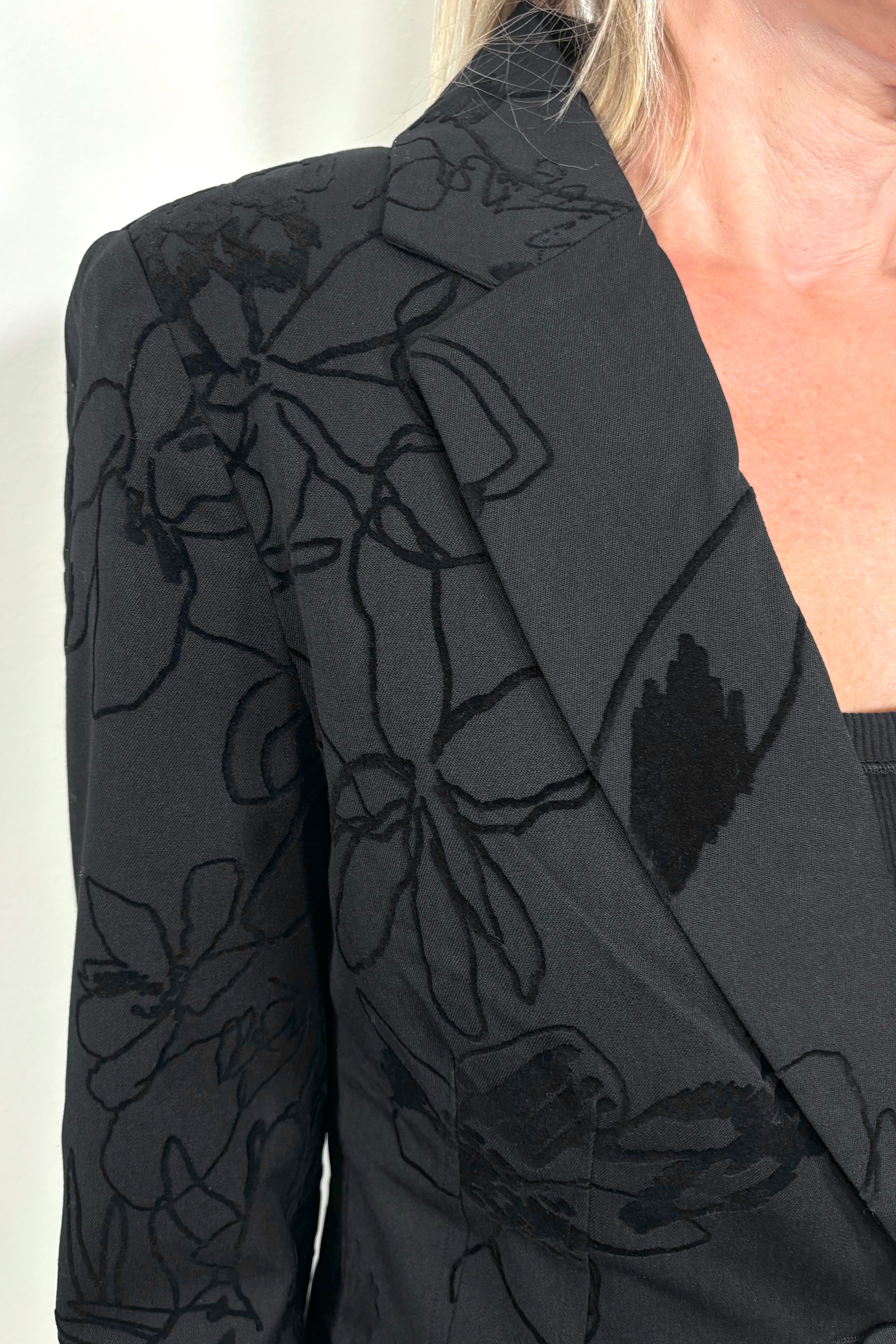 Close up view of woman's right shoulder wearing a black blazer with textures flowers detailing