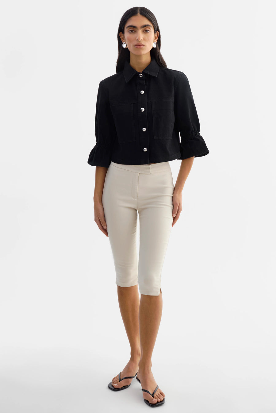 Woman wearing a black jacket with silver buttons and 3/4 sleeves. 