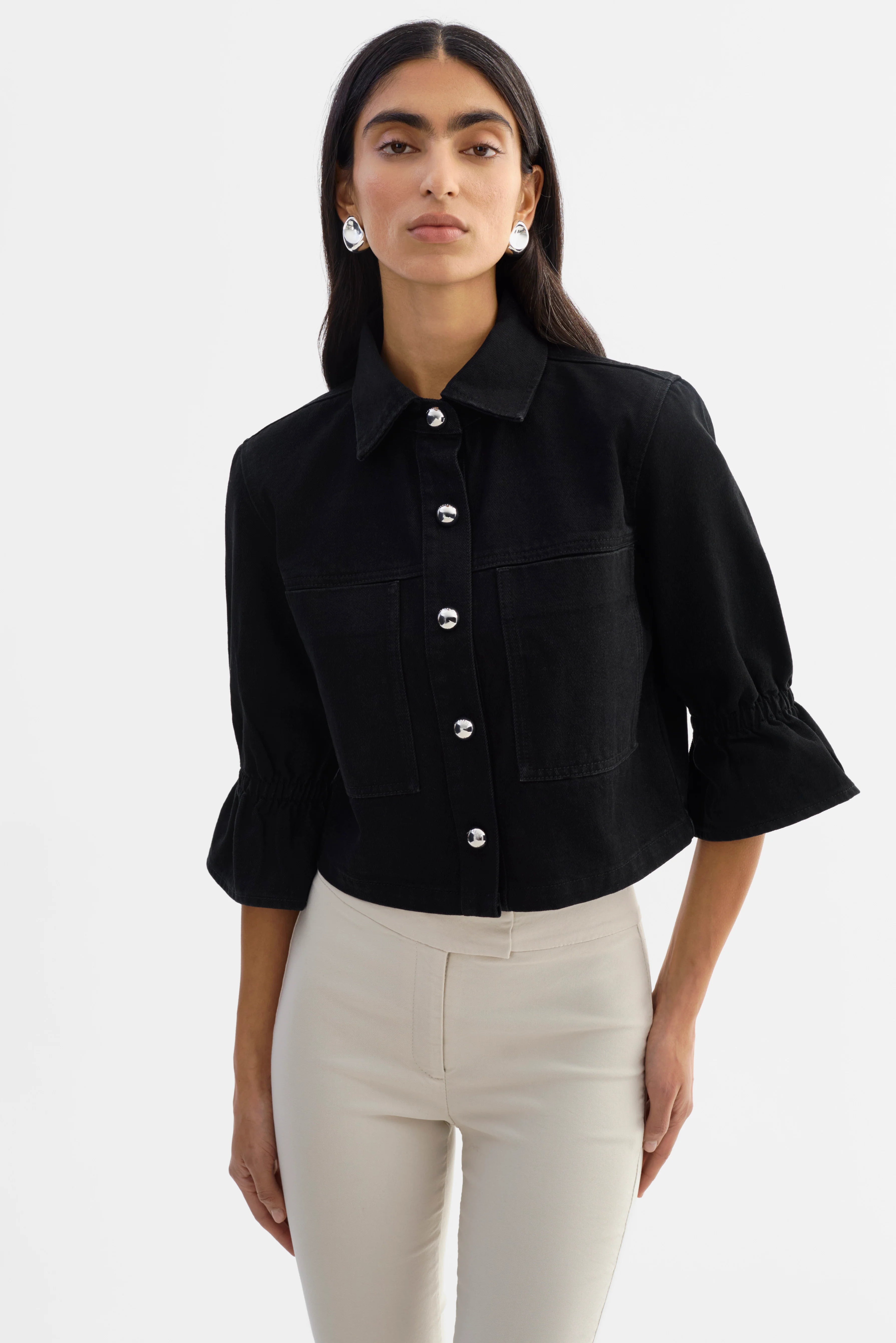 Woman wearing a black jacket with silver buttons and 3/4 sleeves. 