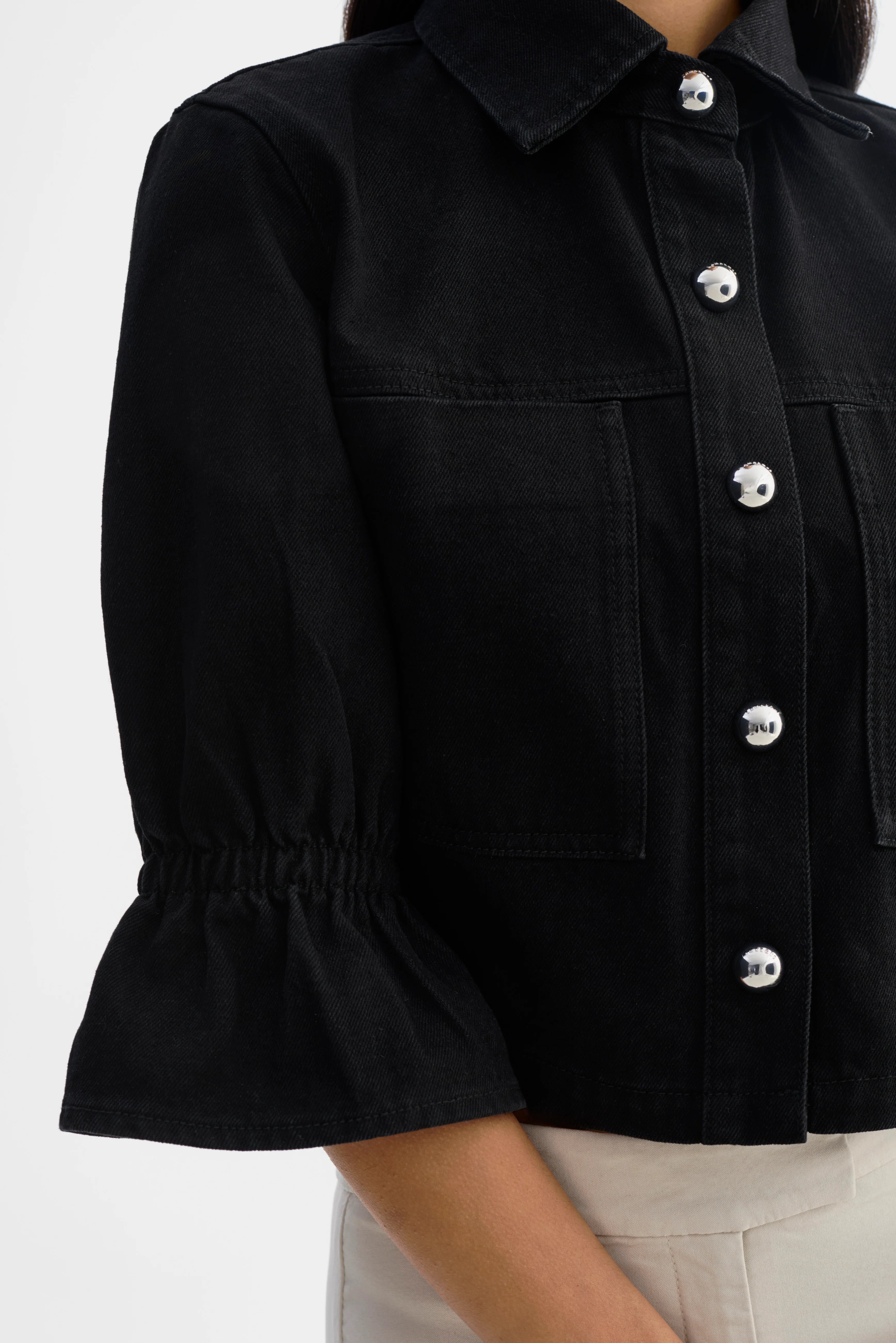 Woman wearing a black jacket with silver buttons and 3/4 sleeves. 