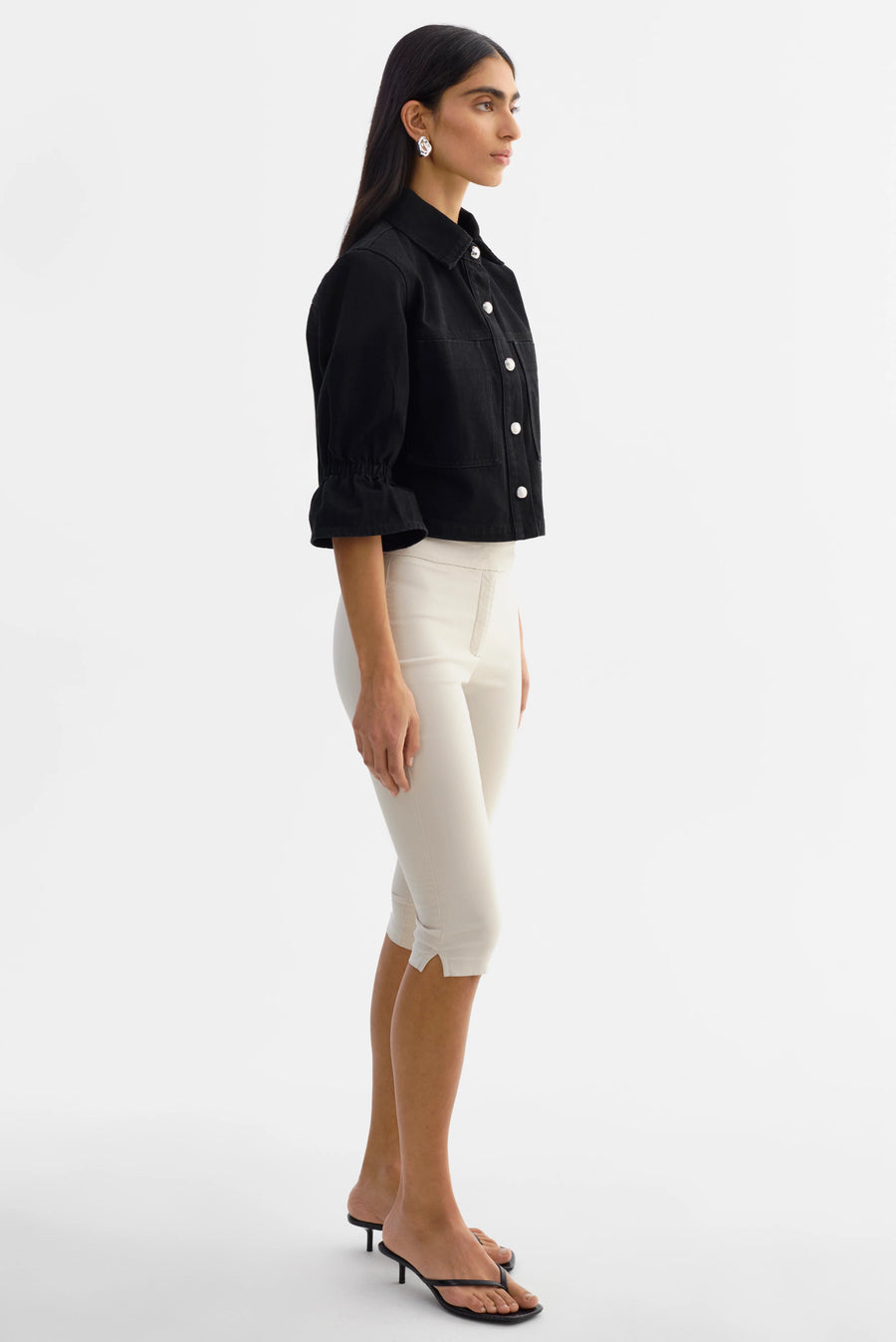 Woman wearing a black jacket with silver buttons and 3/4 sleeves. 