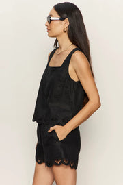 woman wearing a black sleeveless top with wide straps and scalloped hem detailing paired with matching shorts, side