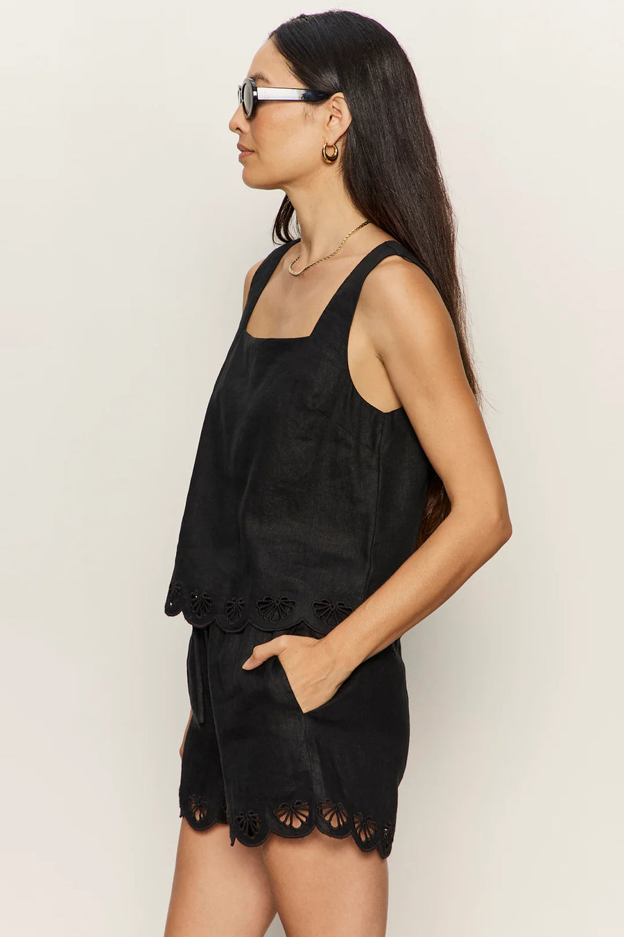 woman wearing a black sleeveless top with wide straps and scalloped hem detailing paired with matching shorts, side