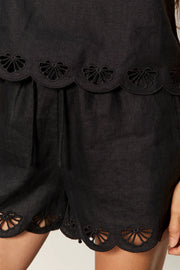 woman wearing a black sleeveless top with wide straps and scalloped hem detailing paired with matching shorts, detail
