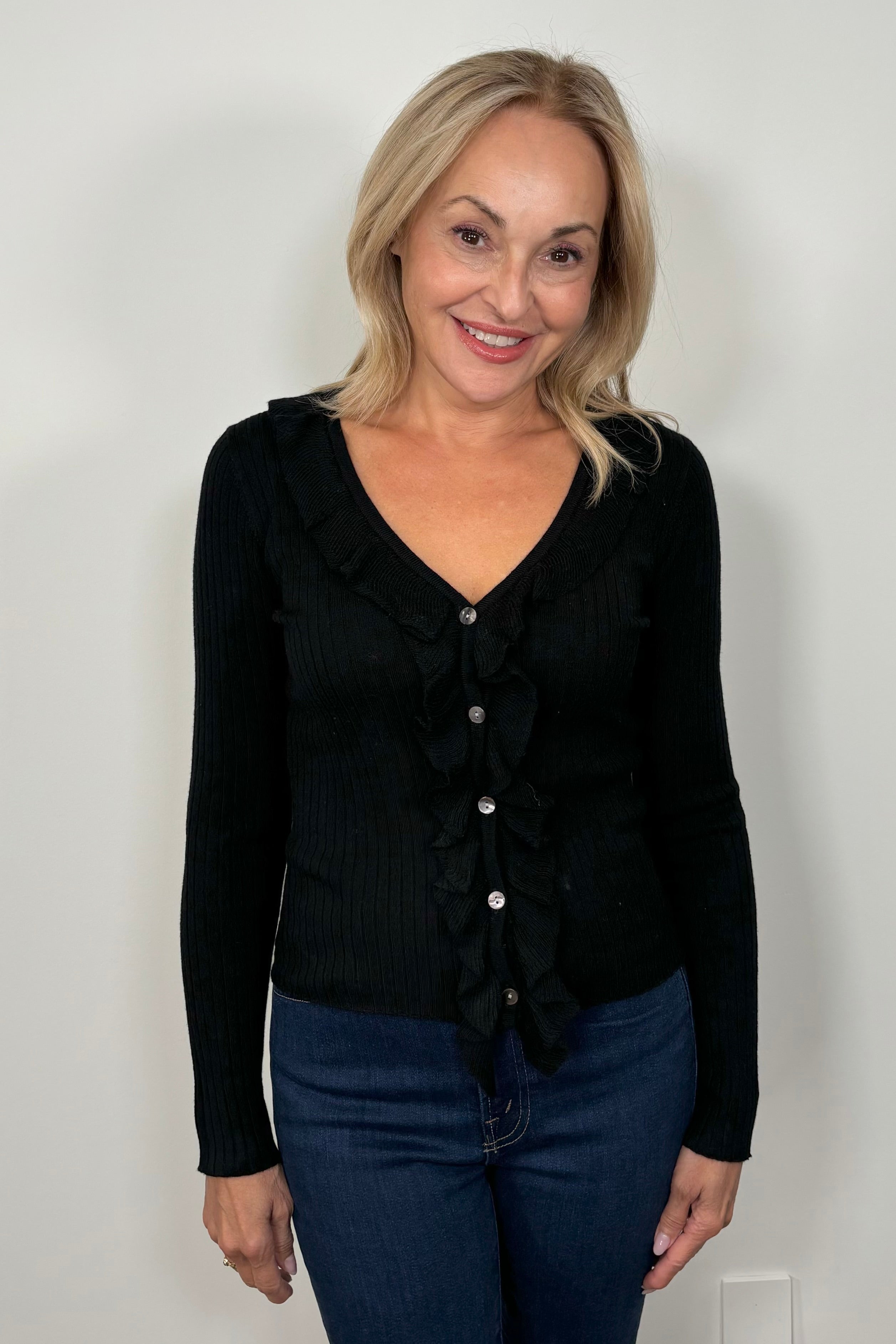 Front facing woman wearing a black v-neck with ruffles long sleeve ribbed top.