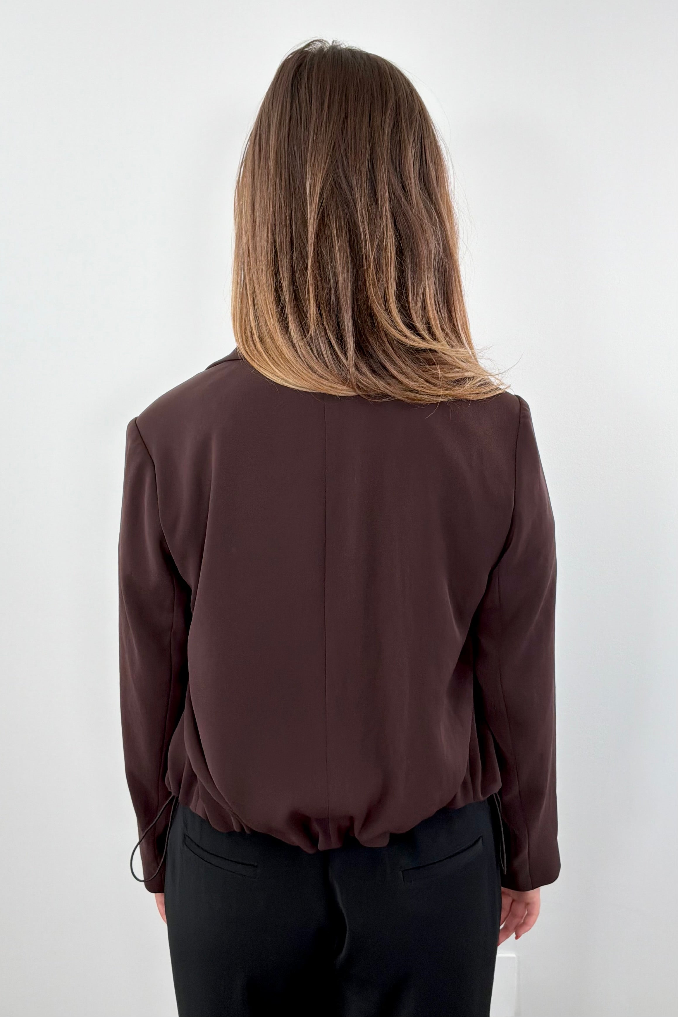 Woman wearing a brown blazer with tie detail at bottom 
