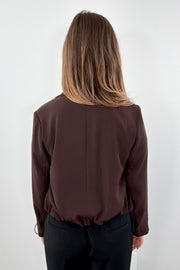 Woman wearing a brown blazer with tie detail at bottom 