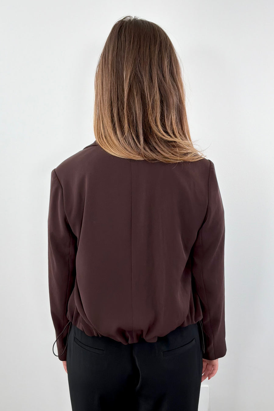 Woman wearing a brown blazer with tie detail at bottom 