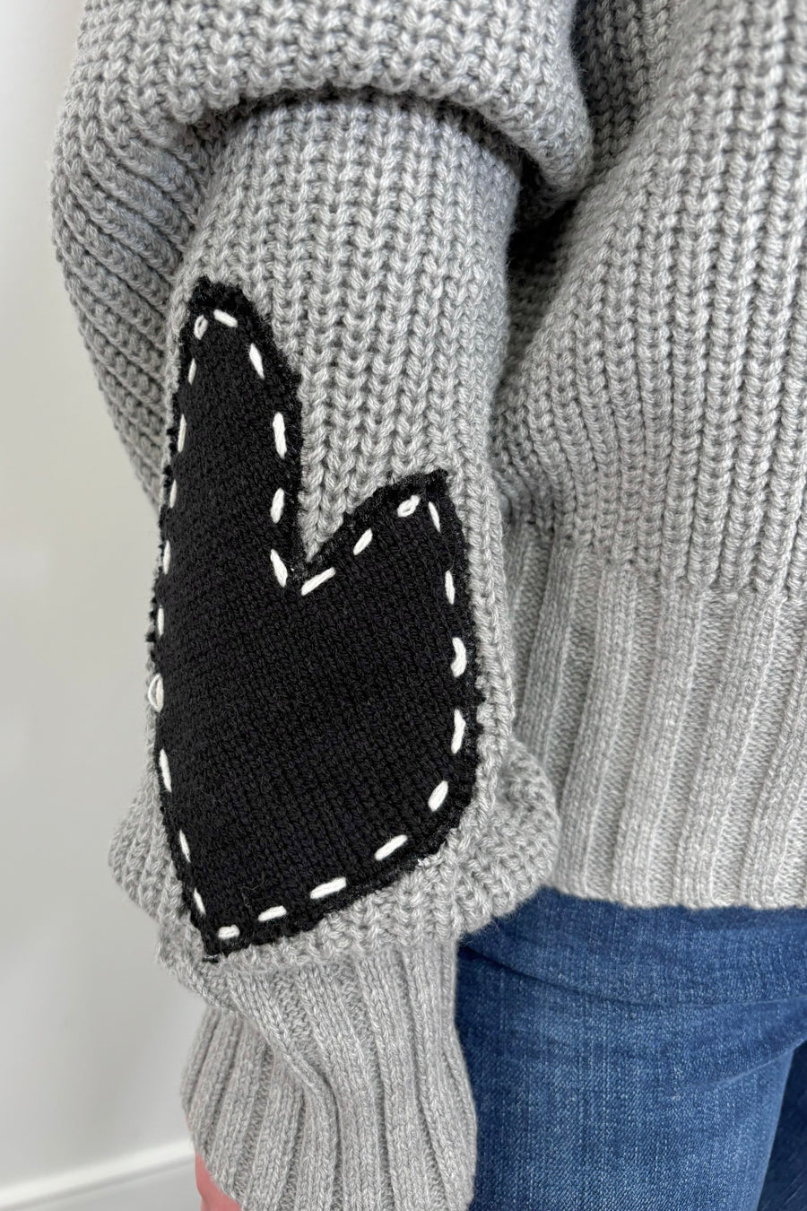 close up view of woman wearing a gray sweater with letter spelling love, hearts in the elbows with whipstitch detailing