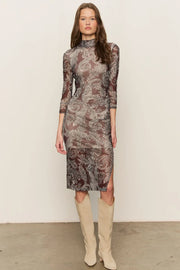 Woman wearing a mesh patterned dress with long sleeves and high neckline, paired with beige knee-high boots on a plain background.