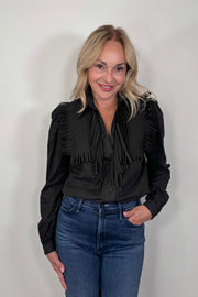 Woman wearing a black long sleeve collared blouse with fringes tucked in