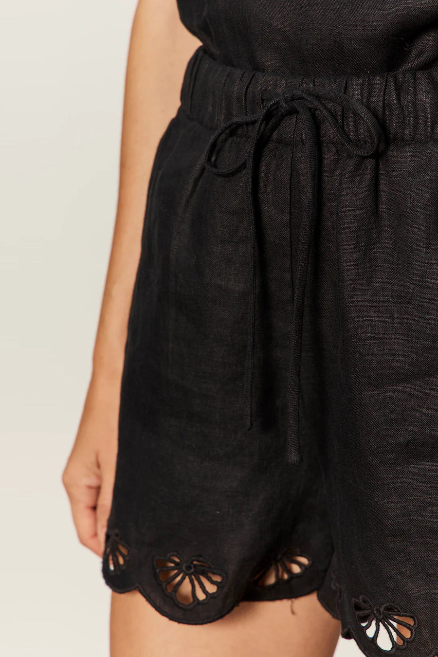 woman wearing black high-waisted shorts with a drawstring waist and scalloped hem detailing, detail