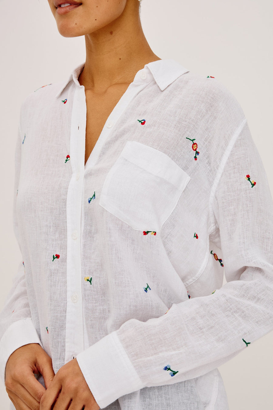 Woman wearing a white button up blouse with flower embroidery 