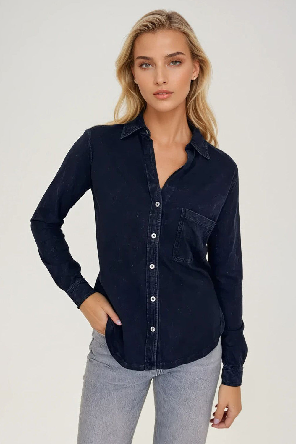 Woman wearing a navy button-up shirt and light blue jeans on a white background