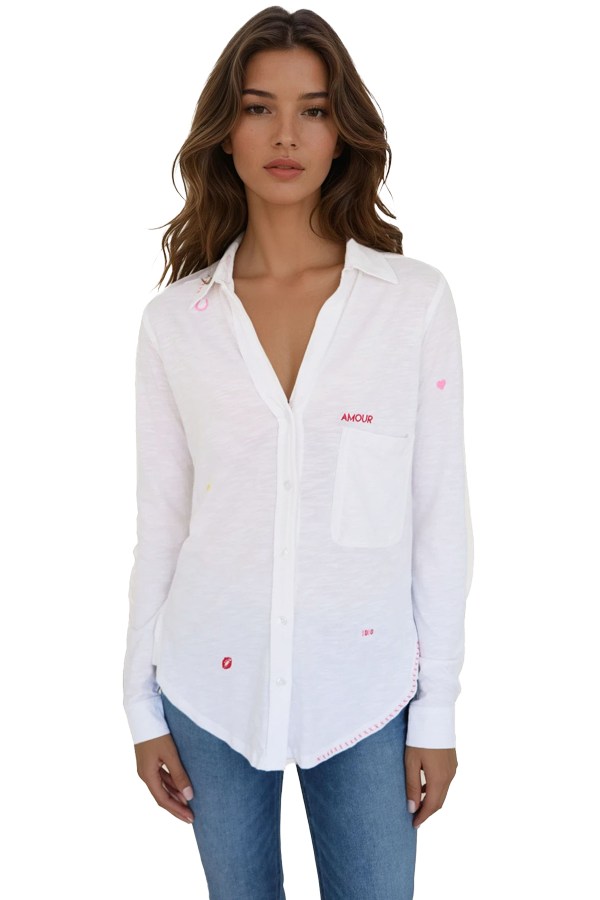 Woman wearing a white button down long sleeve shirt with subtle embroidered heart details and small “AMOUR” text over a front pocket, front view