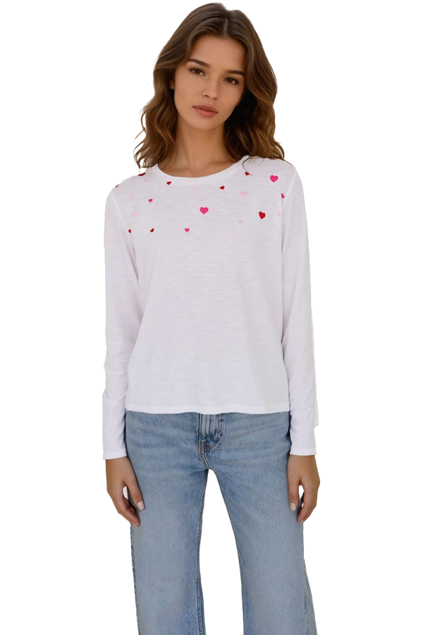 Woman wearing a white long-sleeve crewneck t-shirt with scattered red and pink heart print, front view