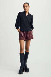 Woman wearing a black blouse with puffed sleeves and burgundy shorts