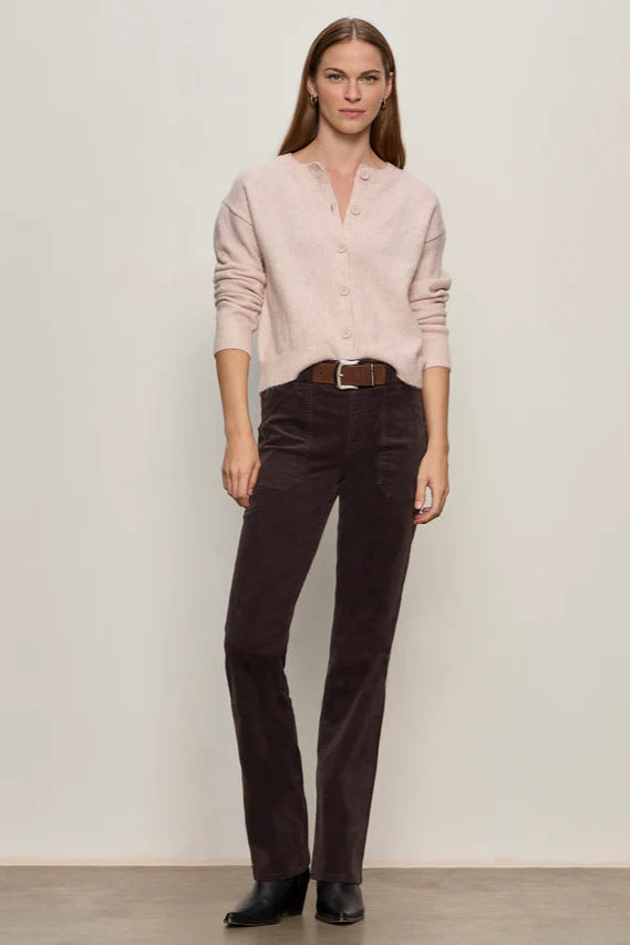 Woman wearing a light pink shirt and dark brown corduroy pants against a plain background