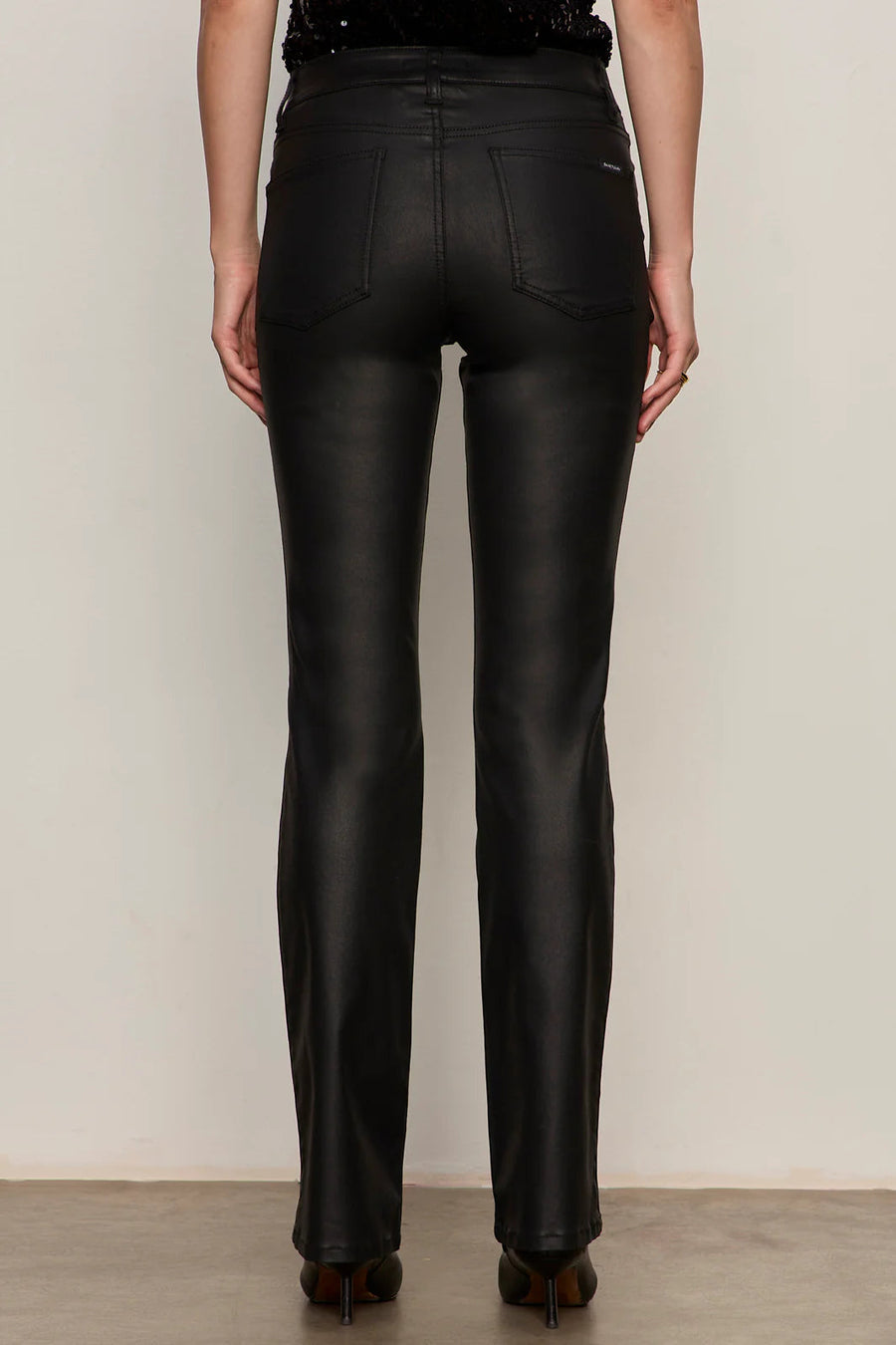 Back view of a person wearing black sculpted denim pants against a plain background