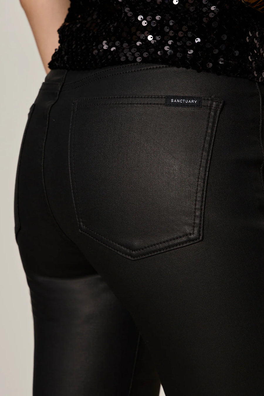 Close up of the back pockets of a person wearing black sculpted denim pants against a plain background