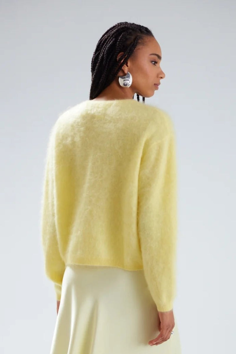 woman wearing a cashmere butter yellow cardigan and skirt on a white background