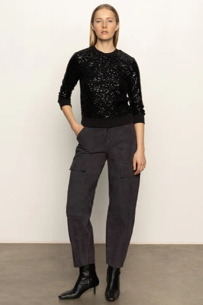 Person wearing a black sequin sweater and dark cargo pants against a plain background