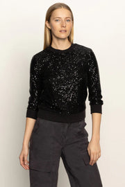 Woman wearing a black sequin sweater and dark pants on a light background