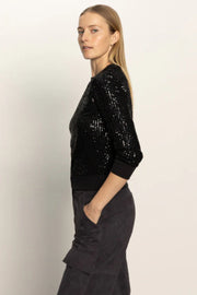 Woman wearing a black sequin top and black pants against a light background