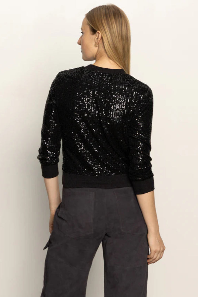 Person wearing a black sequin top and dark pants on a light background