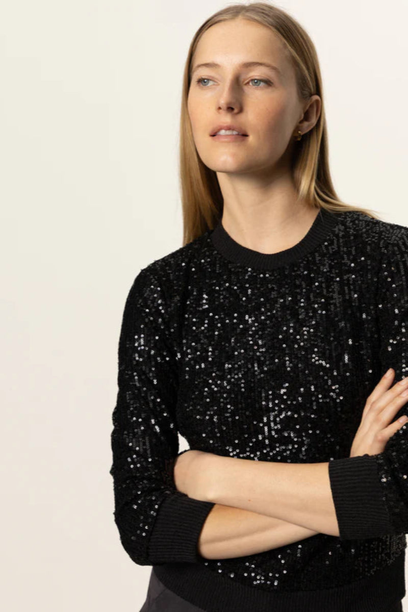 Woman wearing a black sequin sweater against a plain background