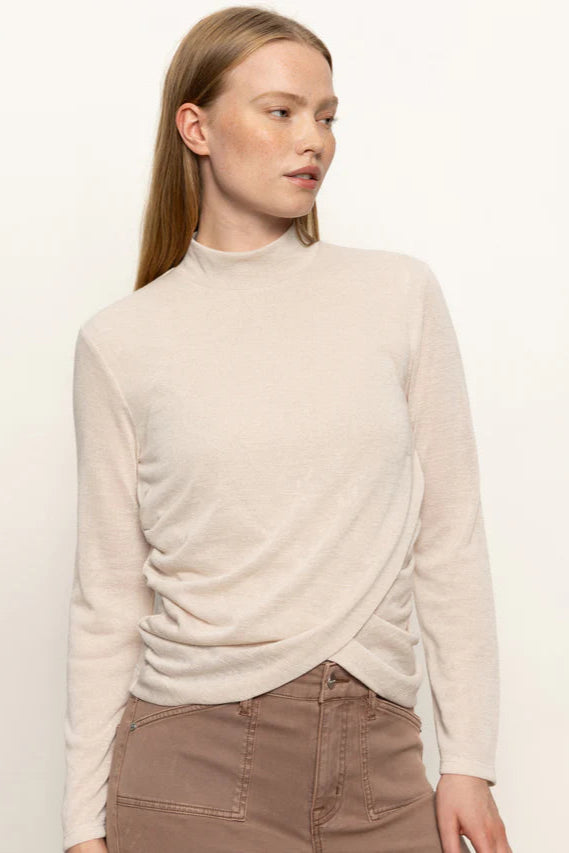 Front view of woman wearing a beige long-sleeve top with rouching in both sides