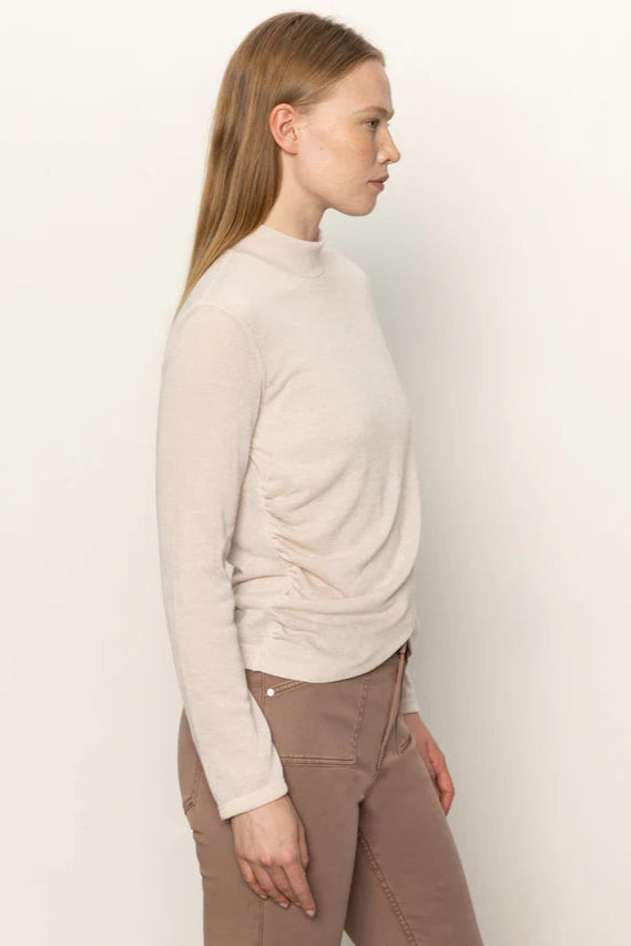 Side view of woman wearing a beige long-sleeve top with rouching in both sides