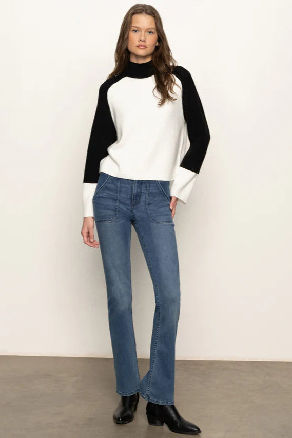 Full body view of a woman wearing a black and white sweater with blue jeans on a plain background
