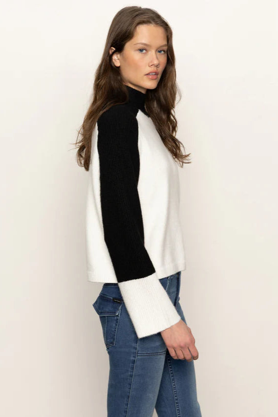 Side view of a woman wearing a black and white sweater with blue jeans on a plain background