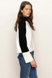 Side view of a woman wearing a black and white sweater with blue jeans on a plain background
