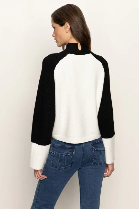 Back view of woman wearing a black and white sweater with blue jeans on a beige background