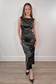Woman wearing a black patterned dress standing against a white wall.