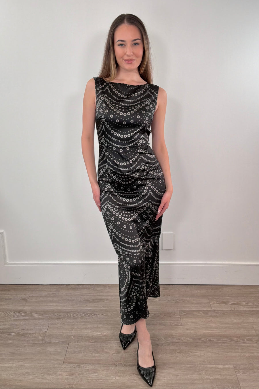 Woman wearing a black patterned dress standing against a white wall.