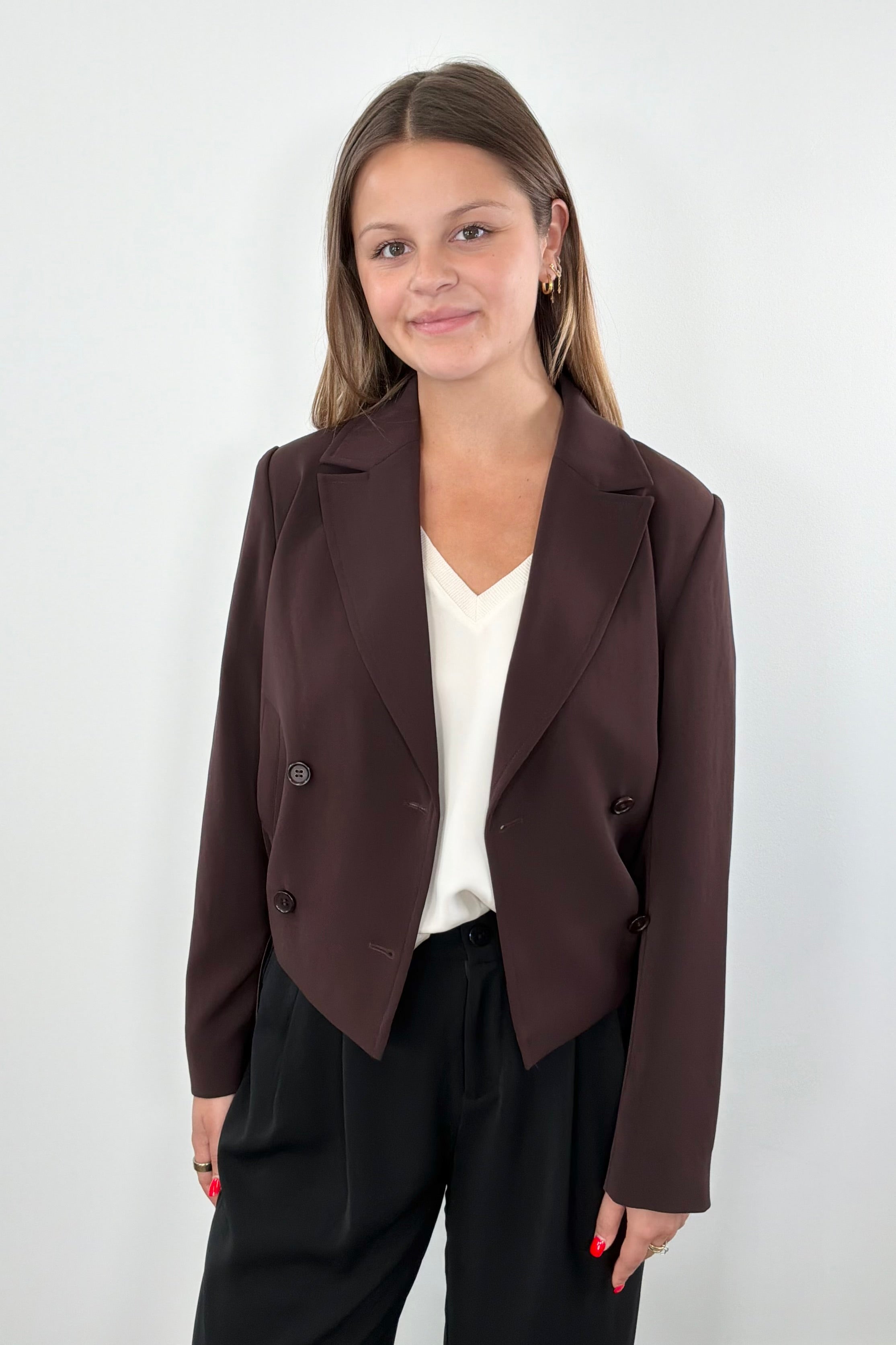 Woman wearing a brown blazer with tie detail at bottom 