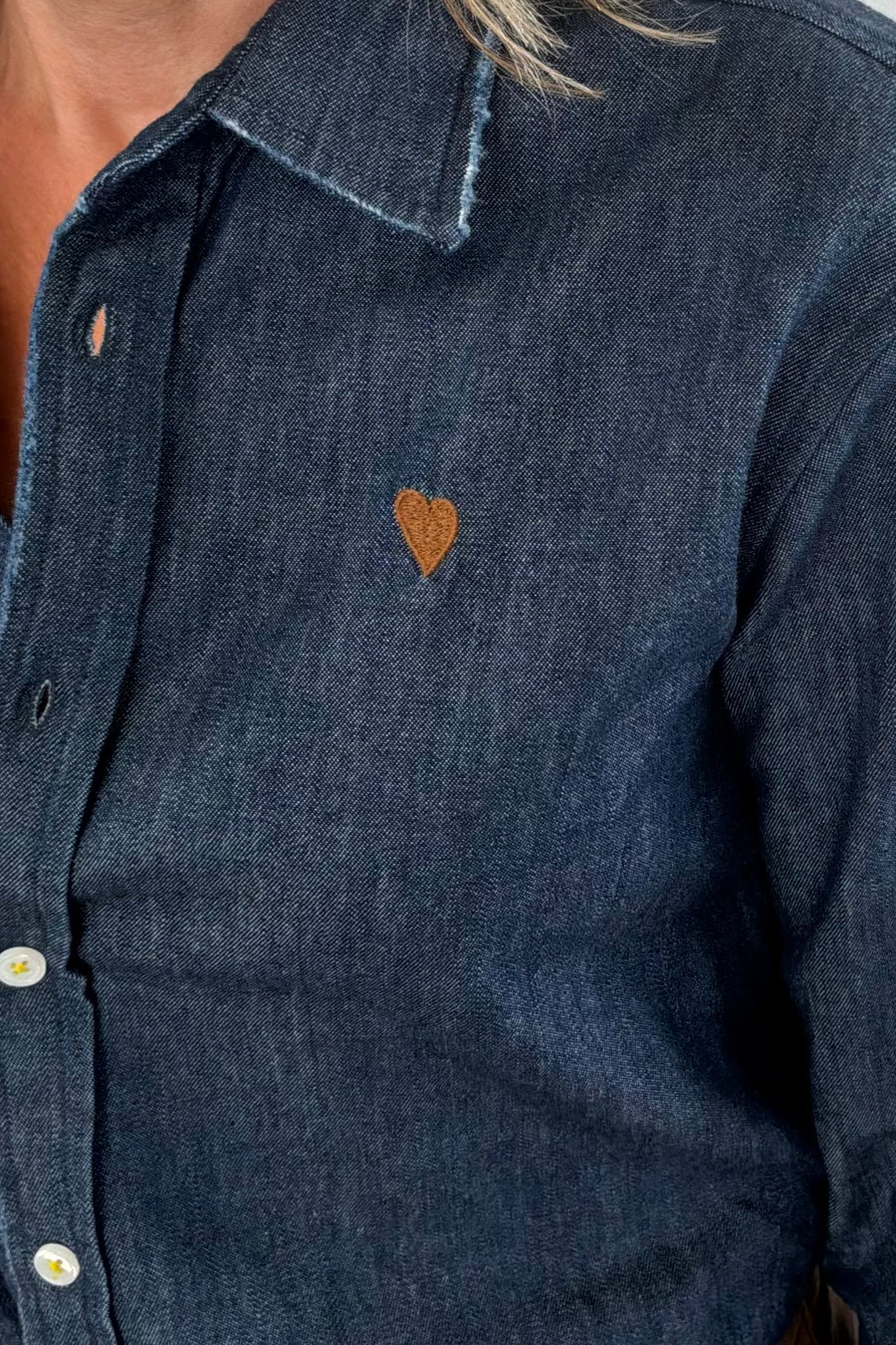 Woman wearing a blue denim shirt with brown heart patches on the elbow