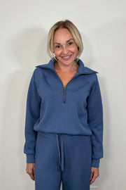 Woman wearing a washed blue zip-up sweatshirt against a light gray background