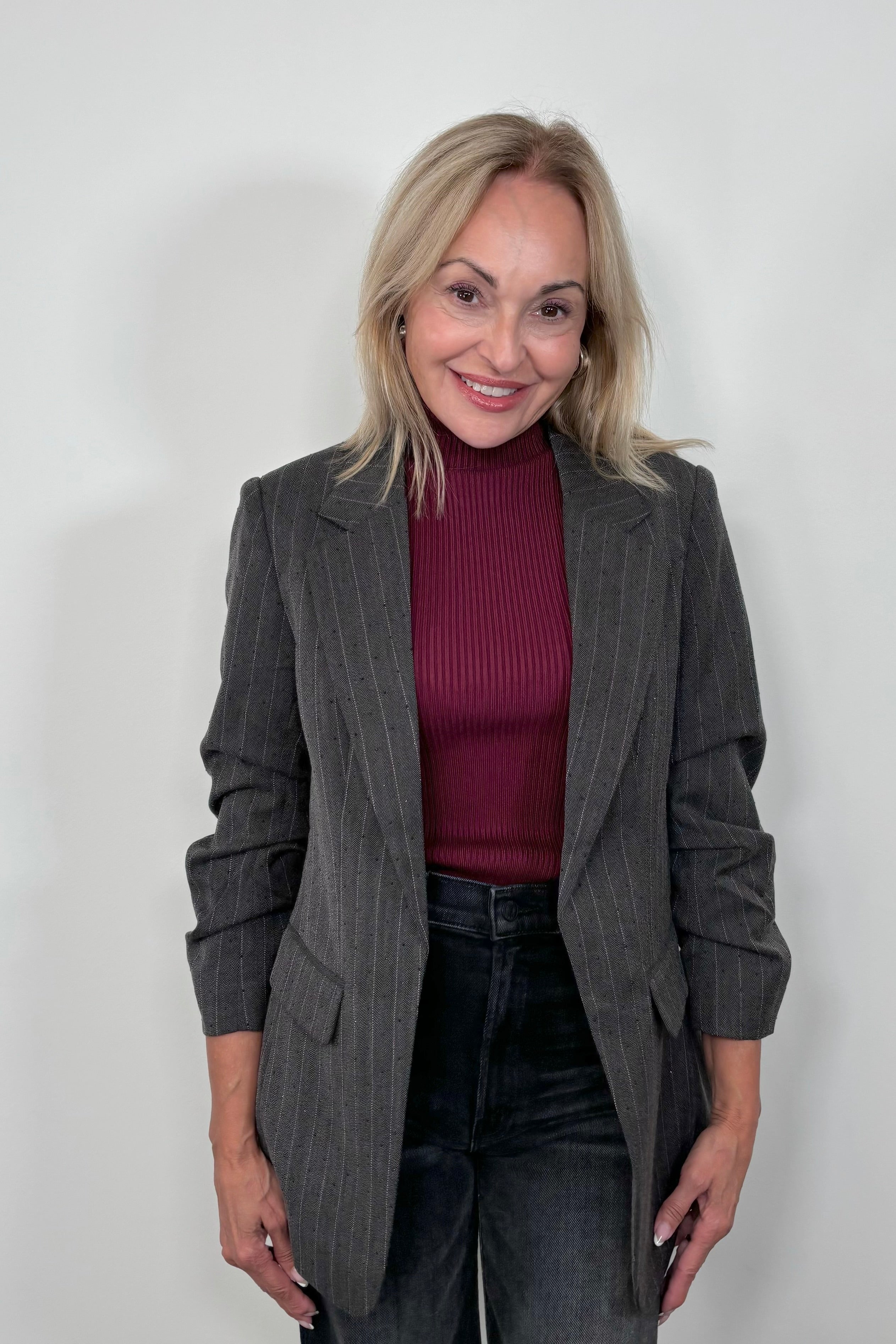 Front view of woman wearing a burgundy turtle neck tank top layered with a gray pinstripe blazer with sparkles