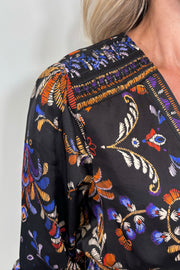 Close up view of woman wearing a satin black v-neck short long sleeve dress with a colourful pattern