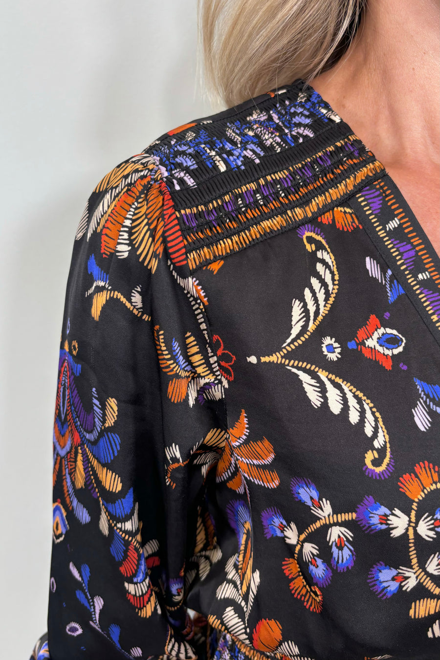 Close up view of woman wearing a satin black v-neck short long sleeve dress with a colourful pattern