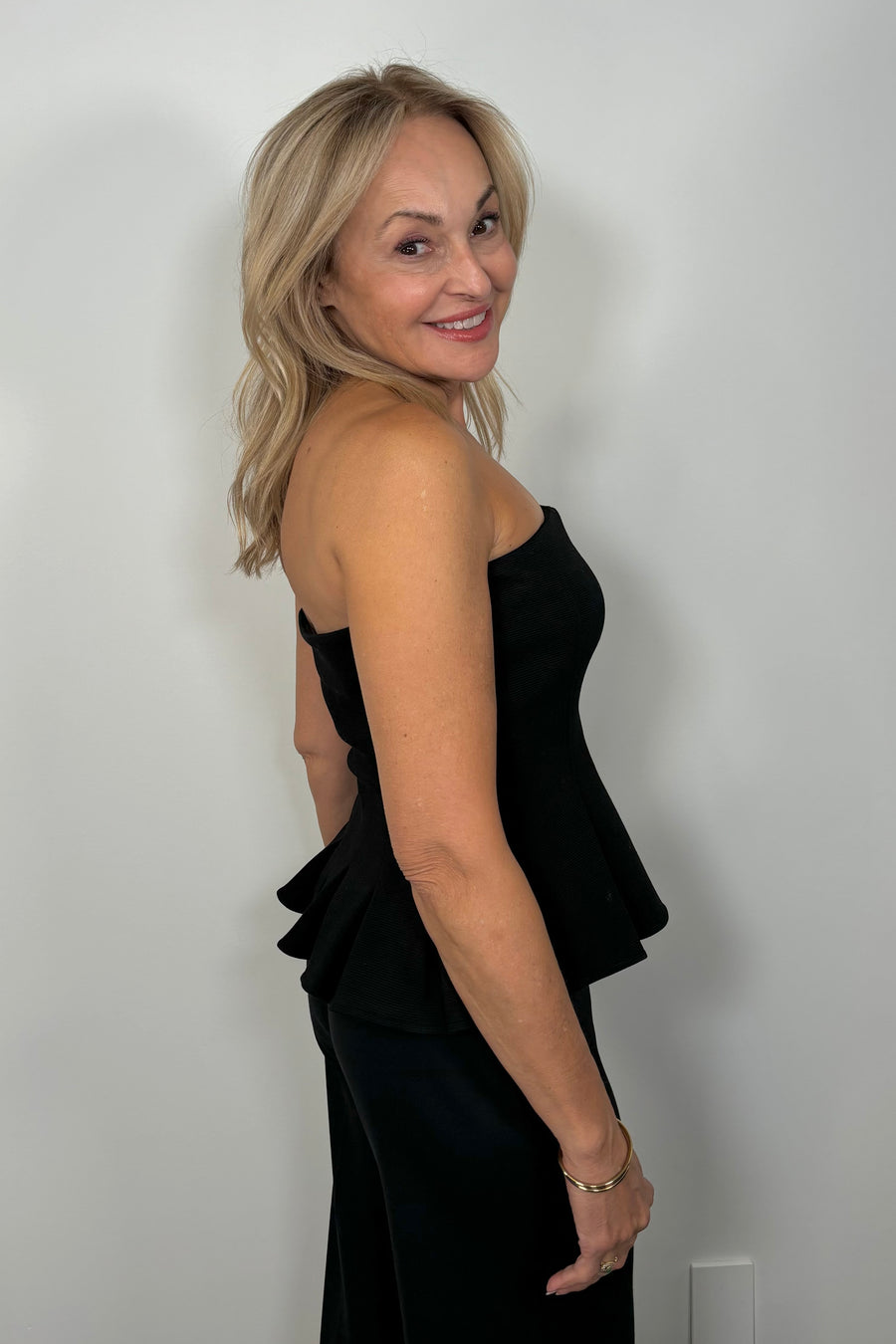 Side view of woman wearing a black pleaded at the bottom strapless top 